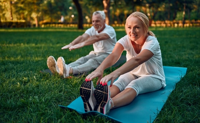Natural Pharmaceuticals „Movisan® Collagen II” Vyresnio amžiaus pora tempiasi pravaikščiodami ant kilimėlio žalioje parko aplinkoje, skatinant sveiką gyvenimo būdą.
