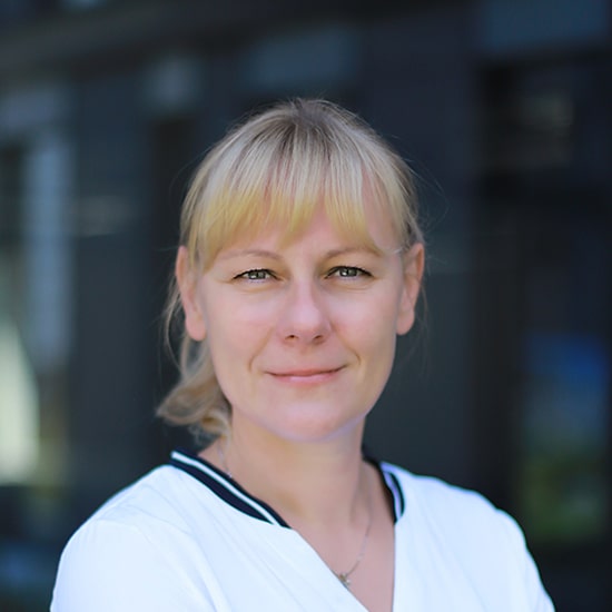 Natural Pharmaceuticals „Movisan® Collagen II” Artimaus plano nuotrauka moters su šviesiais plaukais ir baltu drabužiu, fonas išsiliejęs tamsus.