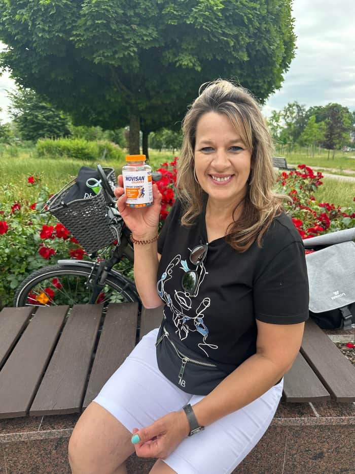 Natural Pharmaceuticals „Movisan® Collagen II” Moterys lauke prie gėlių ir dviračio demonstruoja judėjimą gerinančius Movisan maisto papildus.