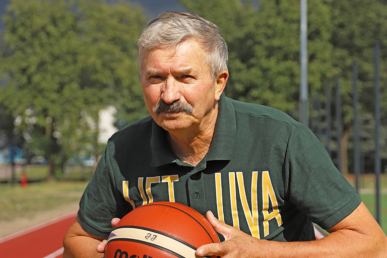 Natural Pharmaceuticals „Movisan® Collagen II” Vyresnio amžiaus vyras žaidžia krepšinį lauke, apsirengęs žalia palaidine su užrašu „LIETUVA“.